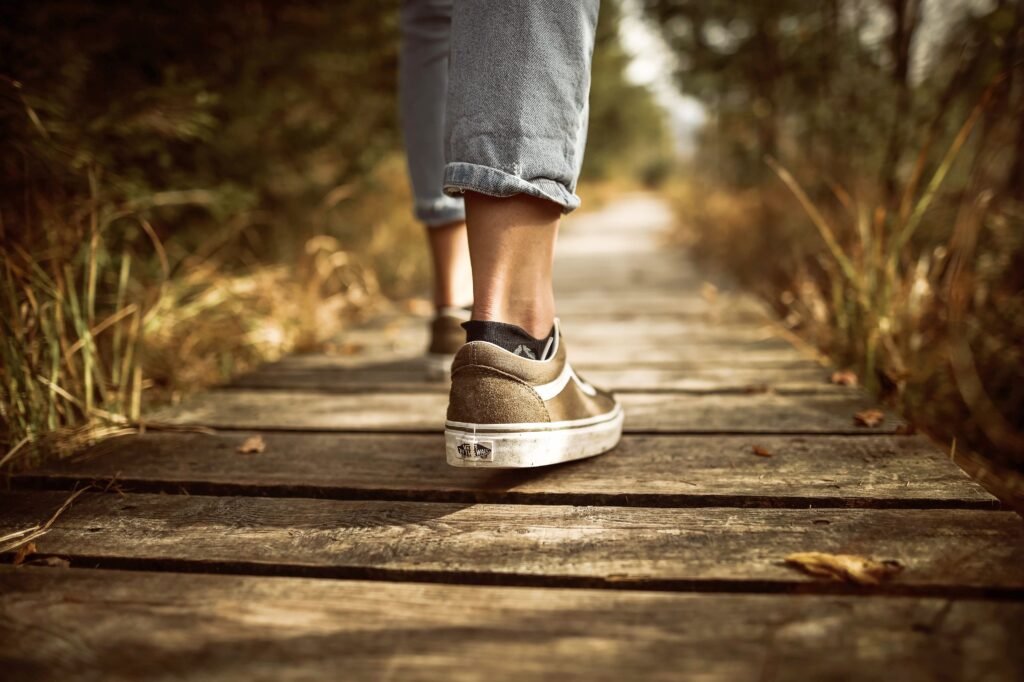 Best Walking Shoes for Men Over 40: 7 Comfortable Picks for Daily Walking Person wearing sneakers walking on a wooden path in a sunlit park.