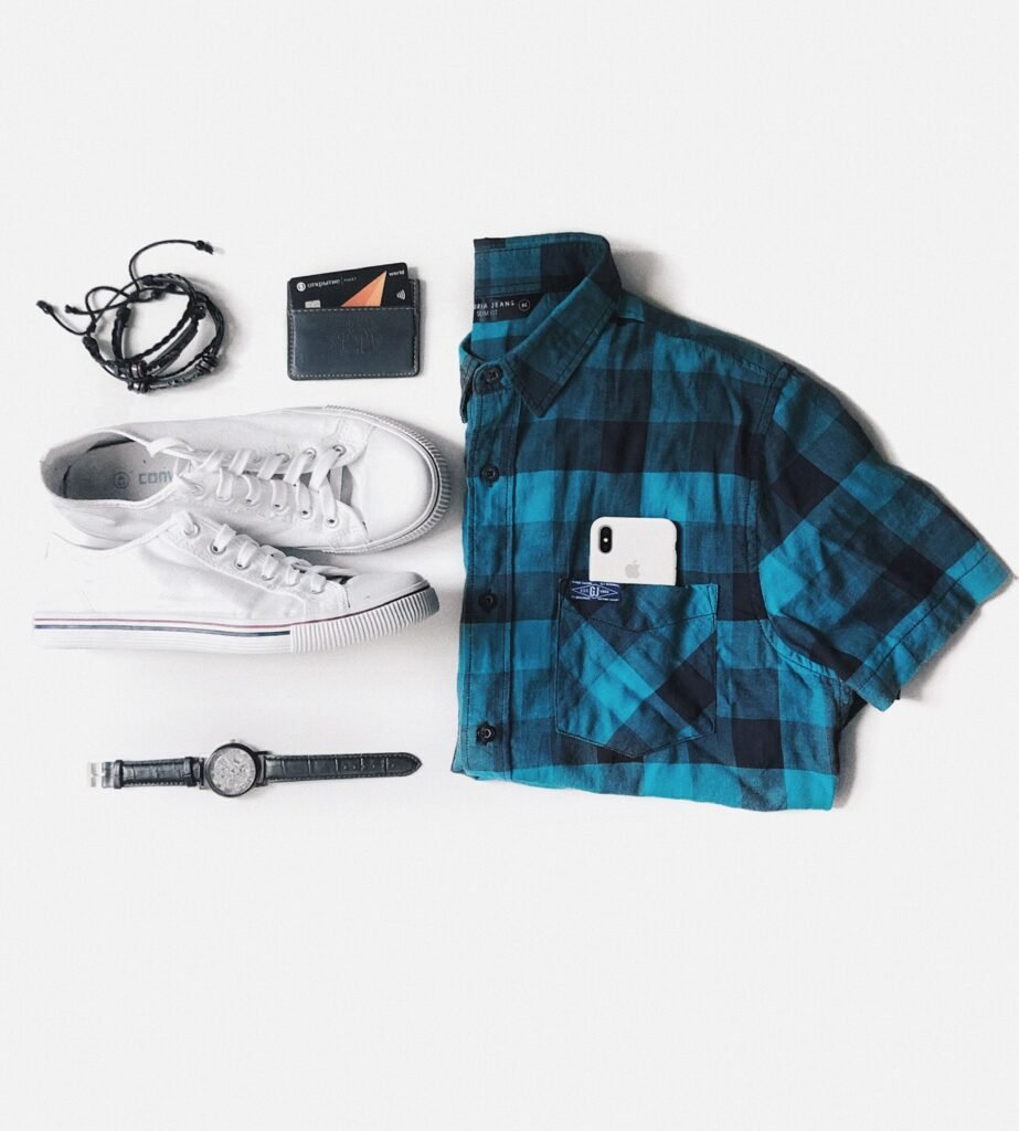 Flat lay featuring a plaid shirt, sneakers, accessories, and wallet on a white background.