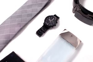 Flat lay of men's fashion items including a watch, tie, belt, and cologne.